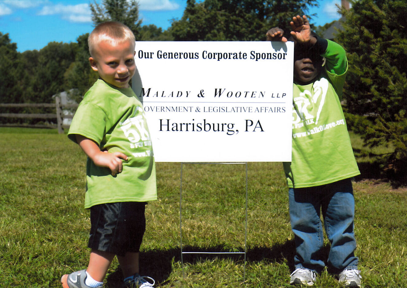 two young boys standing next to a sign that thanks Malady & Wooten government & legislative affairs for their corporate sponsorship